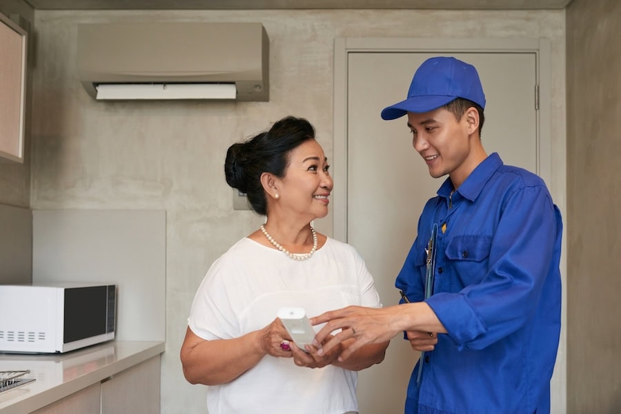 SmiIing technicial explaining Vietnamese senior woman how to use air conditioner remote control.|Girl face expression cooling in front of a fan.