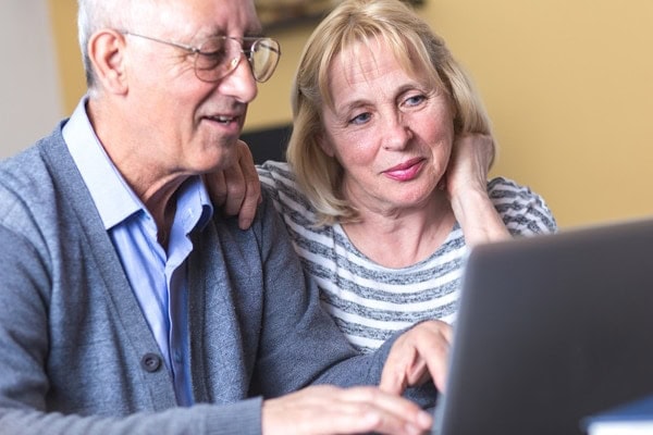 Happy senior couple using laptop at home to go over their utility bills. Multi-stage heat pumps..|